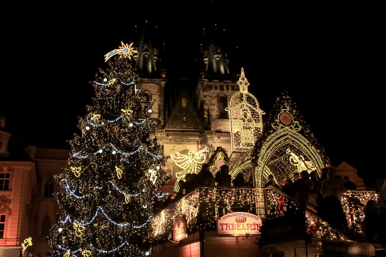 Christmas-market lights and a Trdelnik stall before the floodlit Gothic towers