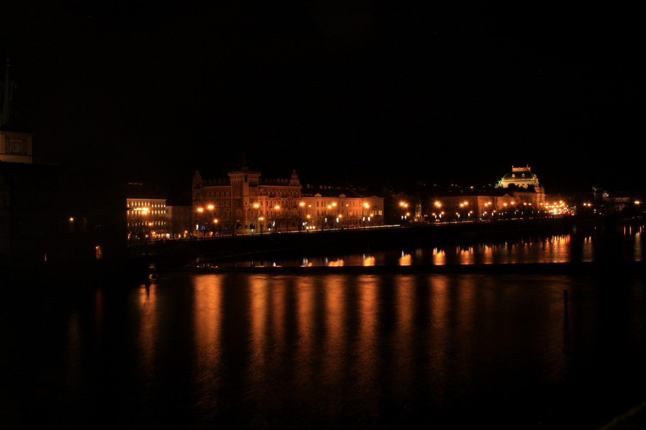 Illuminated waterfront buildings reflected in the dark Vltava at night