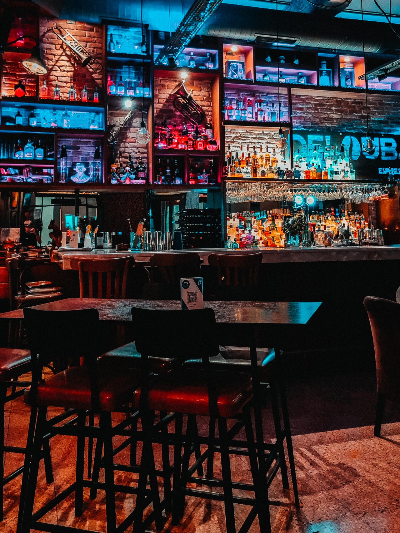 A moody brick-walled cocktail bar under red and blue light
