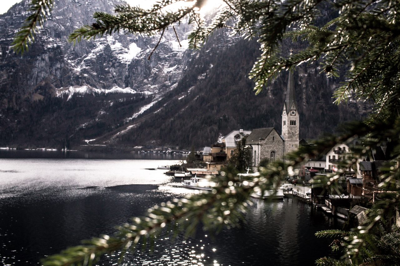 A lakeside church spire framed by pine branches and snow-dusted mountains